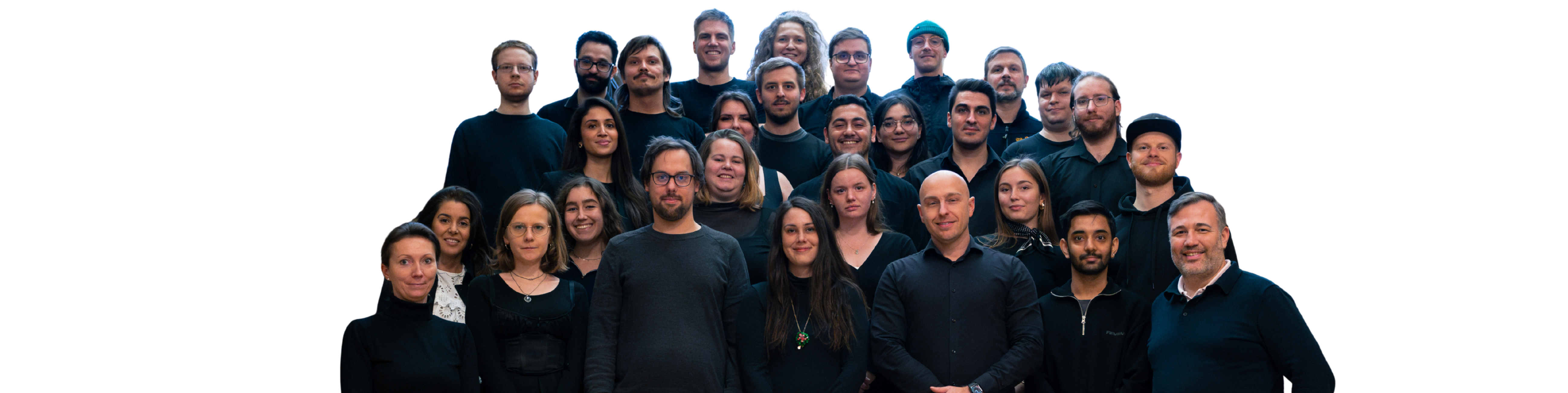Eine Gruppe von 17 Männern und 12 Frauen steht zusammen und lacht in die Kamera. Sie tragen legere, dunkle Alltagskleidung