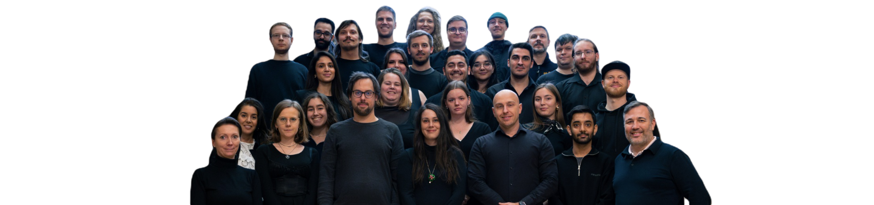 Eine Gruppe von 17 Männern und 12 Frauen steht zusammen und lacht in die Kamera. Sie tragen legere, dunkle Alltagskleidung