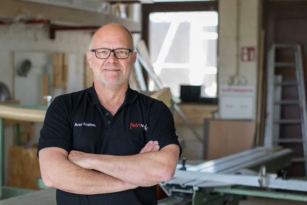 Arne Frahm steht in einer Werkstatt. Frahm Er trägt ein dunkles T-shirt mit Firmenlogo sowie eine Brille